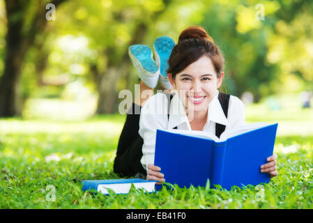 Smiling casual student lying on grass reading book Banque D'Images