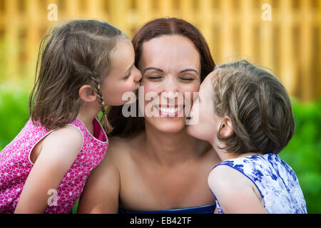 Un portrait photo de famille de deux filles de chaque côté de leur mère, chacun donnant un baiser sur sa joue. Banque D'Images