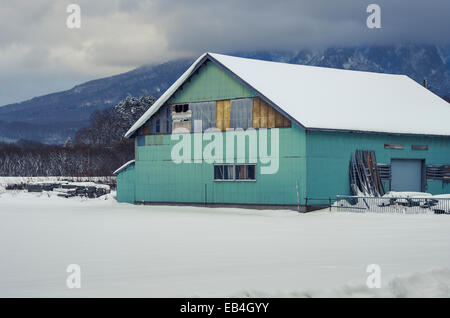 Maison de ferme dans le champ couvert de neige avec nuée couvrait Mt Yotei en arrière-plan. Banque D'Images