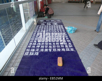 Chine Chinois du continent mère unique écrit sur le sol. calligraphie de sable Elle prétend que sa fille a besoin d'argent pour les tr Banque D'Images