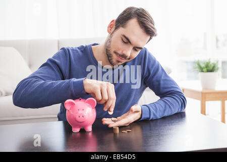 Young man putting coins in piggy bank Banque D'Images