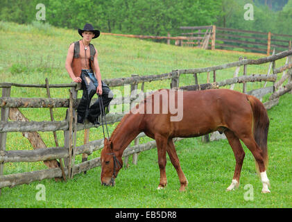 Man in cowboy vêtements assis sur la clôture à côté du cheval Banque D'Images