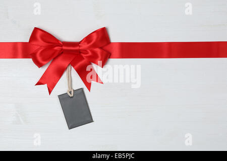 Blank gift tag avec arc et ruban rouge pour les dons sur un fond de bois Banque D'Images