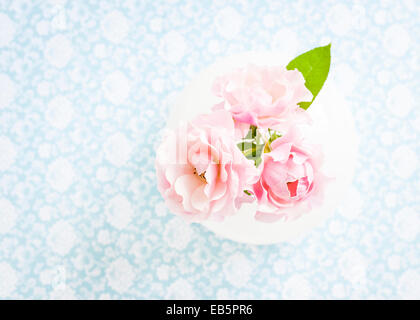 Trois roses roses dans un vase blanc sur un décor floral blanc et bleu Banque D'Images