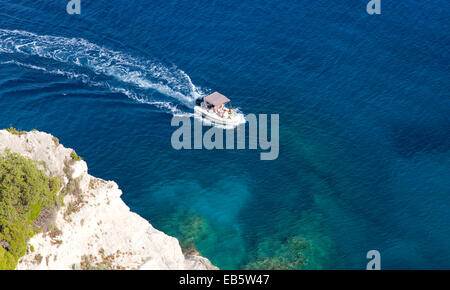 Korithi, Zante, îles Ioniennes, Grèce. Petit bateau passant sous les falaises au-dessus des grottes bleues au Cap Skinari. Banque D'Images