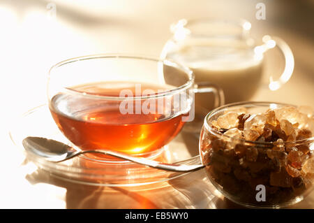 Une tasse de thé, la cassonade dans un bol de sucre en verre et un petit pot à lait Banque D'Images