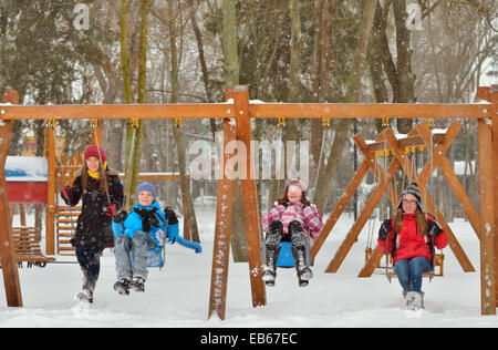 Happy friends sitting on swing dans le parc en hiver Banque D'Images