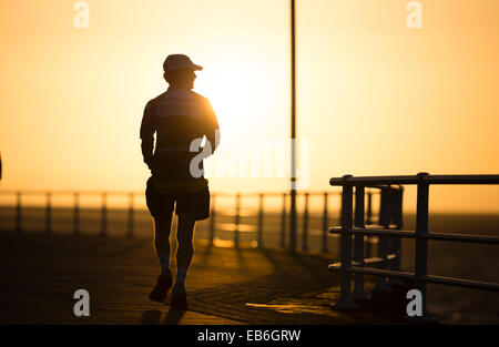 Un homme marche jogging en silhouette au coucher du soleil, par une chaude soirée de septembre, Aberystwyth UK Banque D'Images