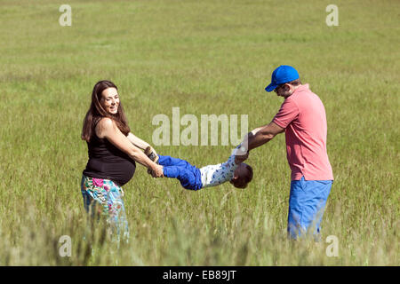 Une famille heureuse, une femme enceinte avec son mari et petit garçon passer du temps ensemble et de jouer à des jeux dans une prairie d'été Banque D'Images