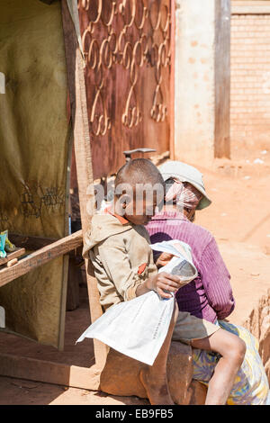Jeune garçon locales africaines travaillant comme exposant en train de lire un journal sur la rue à Antananarivo, ou Tana, capitale de Madagascar Banque D'Images