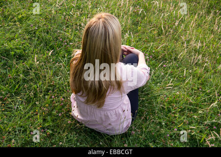 De longs cheveux blond woman sitting on meadow Banque D'Images
