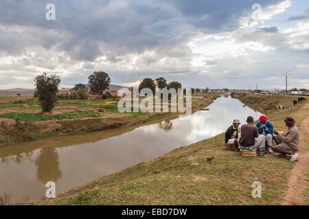 Vie locale : groupe de quatre hommes jouant aux cartes locales africaines sur la rive d'un canal d'irrigation à Antananarivo, ou Tana, capitale de Madagascar Banque D'Images