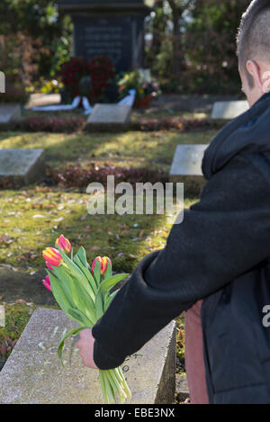 Backview of teenage boy plaçant flowere sur pierre tombale en cimetière, Allemagne Banque D'Images