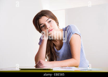 Young woman sitting at desk in office with tablet computer, à la recherche sur le côté et la pensée, de l'Allemagne Banque D'Images