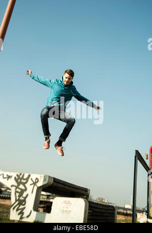 Teenage boy jumping sur banc à l'extérieur, zone industrail, Mannheim, Allemagne Banque D'Images