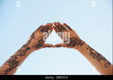 Les mains et les bras de femme peint avec le henné en style arabe, formant Triangle avec vos doigts contre Ciel bleu, Muscat, Oman Banque D'Images