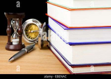 Pile de livres, un stylo et hourglass sur fond noir Banque D'Images