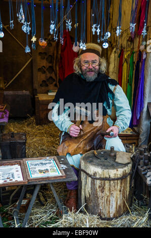 Un homme habillé en costume médiéval pièces de métal de martelage à la main à l'Ludlow castle Noël Nourriture et foire artisanale. Le Shropshire Banque D'Images