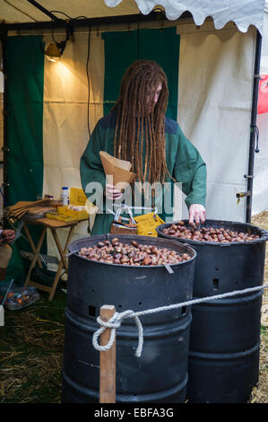 Un homme habillé en costume médiéval la torréfaction et la vente de châtaignes à un décrochage à Ludlow Castle Noël Nourriture et foire artisanale. Banque D'Images