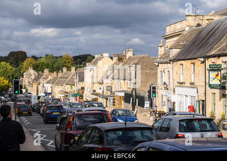 Vue vers le bas de la Grand-rue Burford Oxfordshire en Angleterre avec soleil qui brille sur les bâtiments d'un côté sur un jour nuageux Banque D'Images