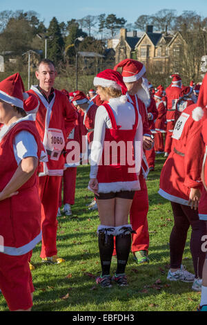 Les personnes (hommes, femmes et enfants) vêtus de rouge et blanc Père Noël Vêtements Chapeaux & fausses barbes, sont debout, attendant de prendre part à la grande Skipton Santa Fun Run, une course de bienfaisance annuelle de collecte de fonds organisé par le Rotary Club Aireville - Park, centre-ville de Skipton, Yorkshire du Nord, Angleterre, Royaume-Uni. Banque D'Images