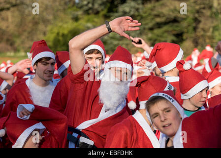 Les personnes (hommes, femmes et enfants) vêtus de rouge et blanc Père Noël Vêtements Chapeaux & fausses barbes, sont debout, attendant de prendre part à la grande Skipton Santa Fun Run, une course de bienfaisance annuelle de collecte de fonds organisé par le Rotary Club Aireville - Park, centre-ville de Skipton, Yorkshire du Nord, Angleterre, Royaume-Uni. Banque D'Images