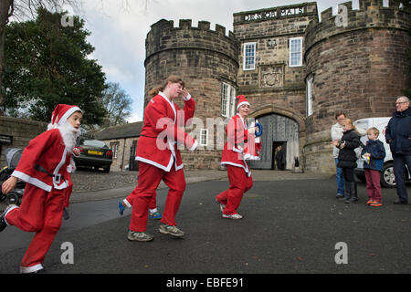 Personnes (femmes et enfants) habillé en rouge et blanc Le Père Noël tenues sont la marche, le jogging, la course et de prendre part à la grande Skipton Santa Fun Run, une course de bienfaisance annuelle de collecte de fonds organisé par le Rotary Club - Château gatehouse, Skipton, Yorkshire du Nord, Angleterre, Royaume-Uni. Banque D'Images