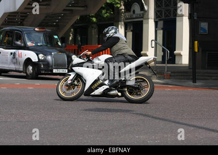 Un motard en tournant à droite sur une route de Londres. Un taxi attend à un ensemble de feux de circulation. Banque D'Images