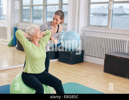 Mature Woman working out sur une balle de remise en forme avec l'aide de l'entraîneur personnel à la salle de sport. Happy senior woman instructor Banque D'Images