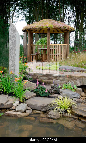 Un joli jardin d'eau avec pont de grès et un pavillon d'été en bois avec un toit Sedum Banque D'Images