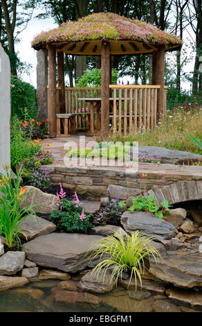 Un joli jardin d'eau avec pont de grès et un pavillon d'été en bois avec un toit Sedum Banque D'Images
