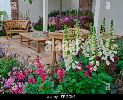 Un jardin contemporain avec terrasse et un élégant mobilier en bois entouré de fleurs colorées frontières Banque D'Images