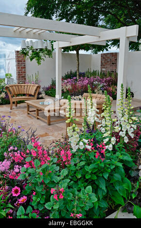 Un jardin contemporain avec terrasse et un élégant mobilier en bois entouré de fleurs colorées frontières Banque D'Images