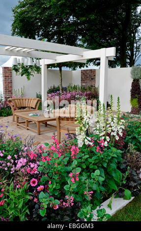 Un jardin contemporain avec terrasse et un élégant mobilier en bois entouré de fleurs colorées frontières Banque D'Images