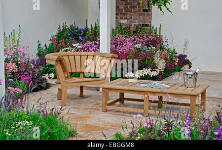 Un jardin contemporain avec terrasse et un élégant mobilier en bois entouré de fleurs colorées frontières Banque D'Images