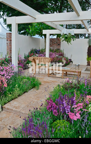 Un jardin contemporain avec terrasse et un élégant mobilier en bois entouré de fleurs colorées frontières Banque D'Images