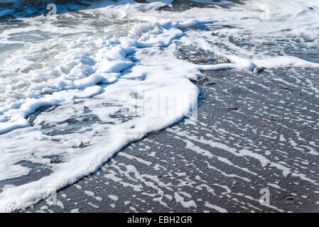 La plage, la mer, baignée par la mer de sable mousse des vagues au lever du soleil Banque D'Images
