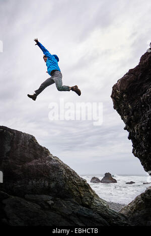 Homme sautant par-dessus les rochers, Prairie Creek Redwoods State Park, Californie, États-Unis Banque D'Images