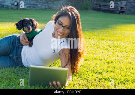 Young woman lying on grass using digital tablet with pet dog