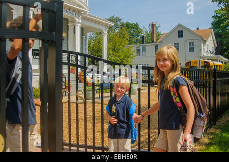 La main d'écolière avec son jeune frère à l'école gate Banque D'Images