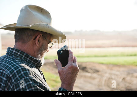 Plus d'épaule de senior male farmer holding up smartphone, Plattsburg, New York, USA Banque D'Images