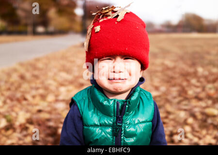 Portrait of male toddler avec feuilles d'automne sur red hat tricoté Banque D'Images