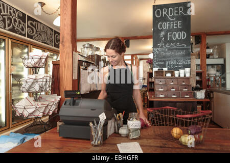 Female Sales assistant à l'aide de check out jusqu'à country store cafe Banque D'Images
