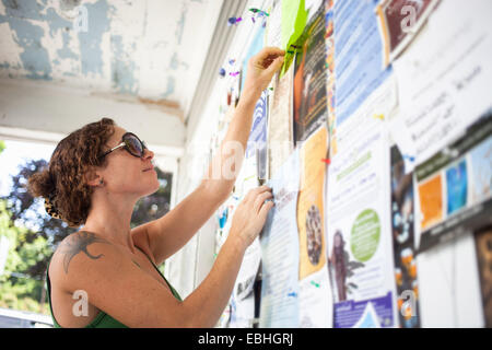 Mid adult woman pinning up avis sur tableau d'affichage communautaire Banque D'Images