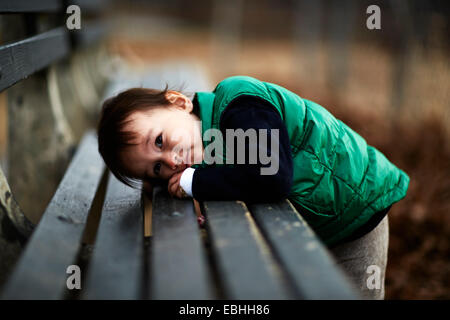 Portrait of male toddler penchée en avant sur le banc de parc Banque D'Images