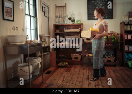 Femme shop assistant transportant des caisses de fruits et légumes en magasin Banque D'Images