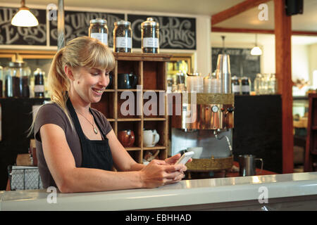 Femme shop assistant texting on smartphone in country store cafe Banque D'Images