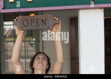 Femme shop assistant atteindre pour ouvrir signe à country store Banque D'Images