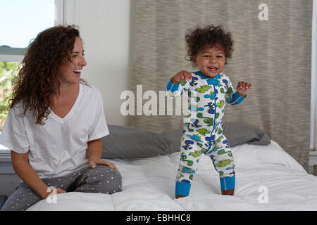 Jeune femme regardant petit garçon jumping on bed Banque D'Images