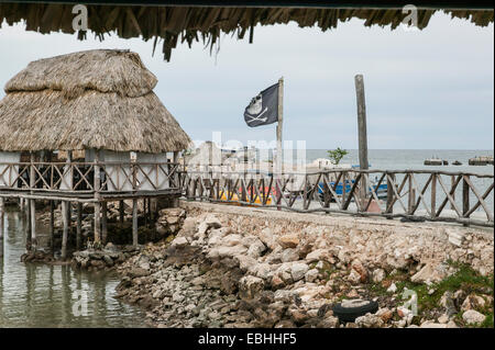 Toit de chaume patio salle à manger surélevée au-dessus de l'eau avec drapeau pirate en lambeaux dans le vent, dans la baie de Campeche, Campeche, Mexique. Banque D'Images